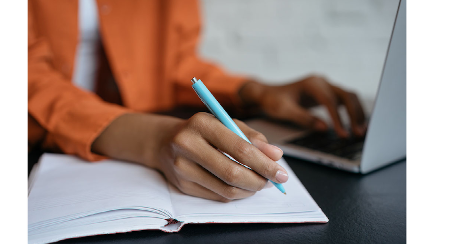 Person writing on paper and typing on a computer