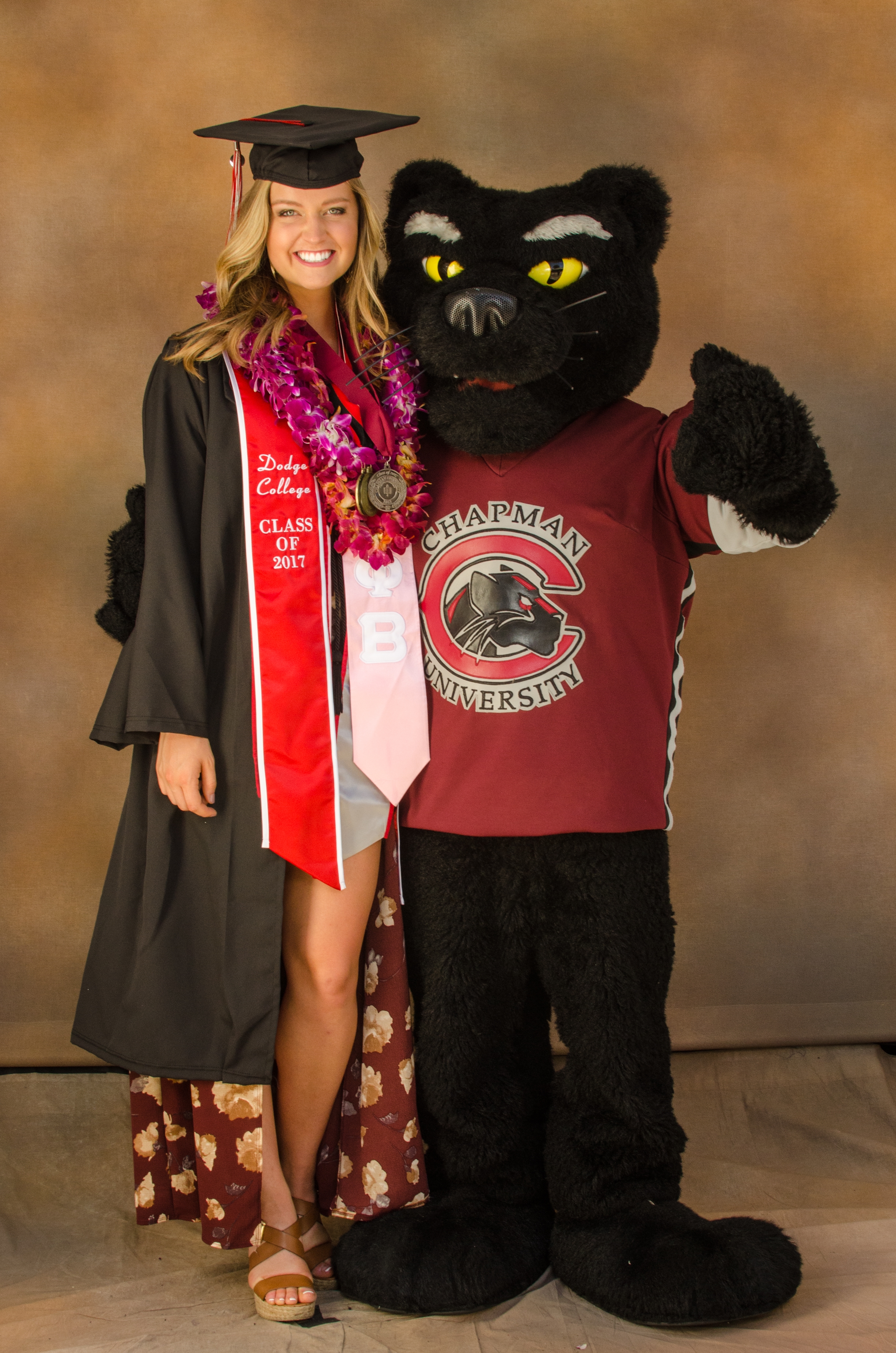 Woman in graduation cap and gown stands next to mascot of a panther.