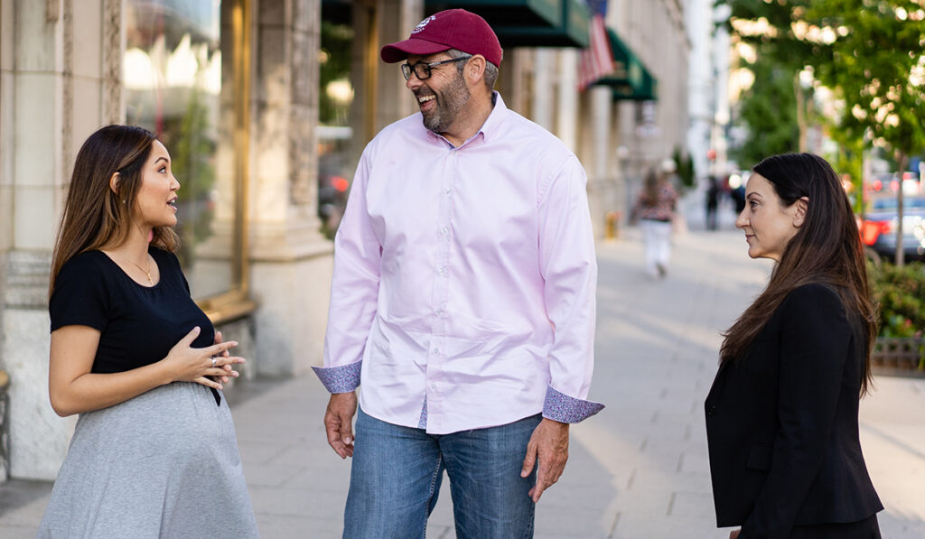 three students talking and laughing on sidewalk