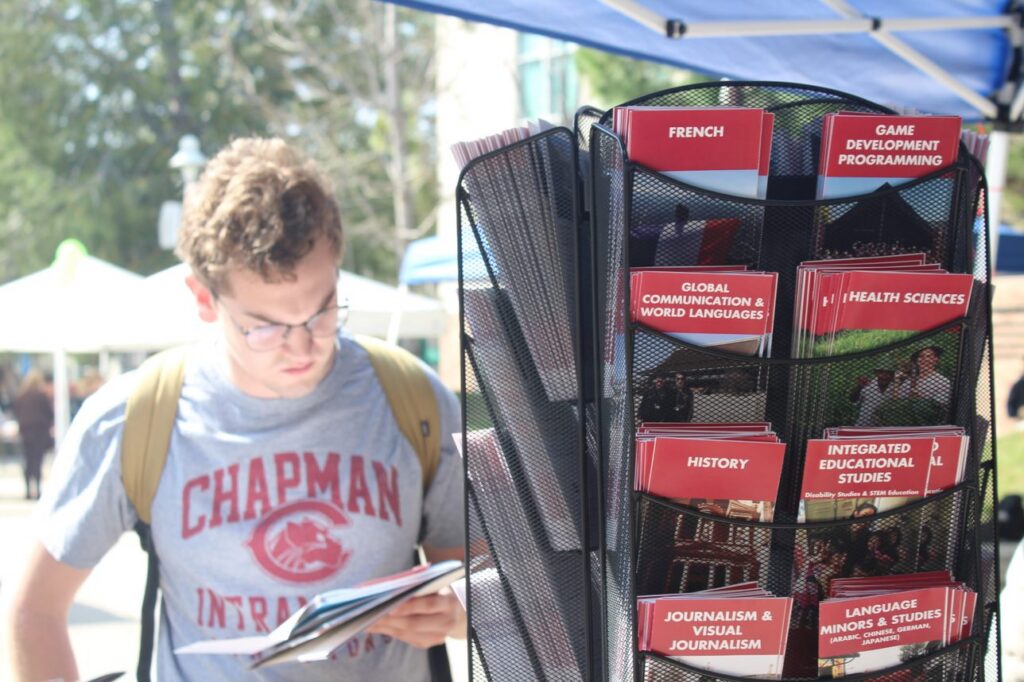 Student reading brochure, standing next to mobile shelf of other brochures with majors listed at study abroad fair.