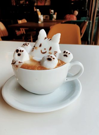 A cute coffee. White coffee cup on white place. Seemingly marshmallows on top of the coffee cup in the shape of a bunny taking a bath in the coffee.