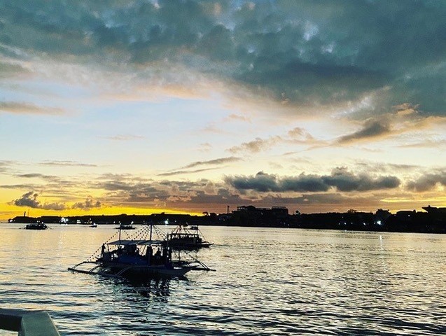 The ocean while the sun is setting. Some boats are spread out across the water and the water looks dark.
