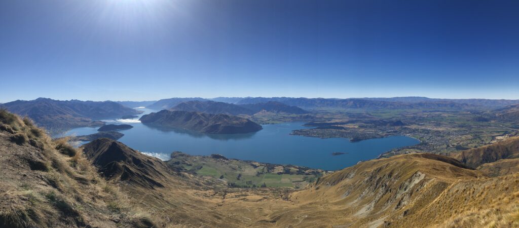 Panoramic photo of New Zealand including a lake with dark blue water and several small islands throughout.