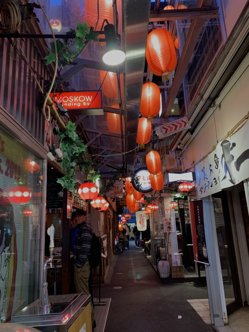 Nightime narrow street with retailers on both sides.