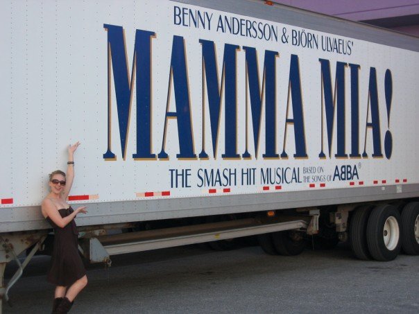 Woman standing next to truck with Mamma Mia! logo.
