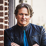 Man with arms crossed leaning on brick wall.