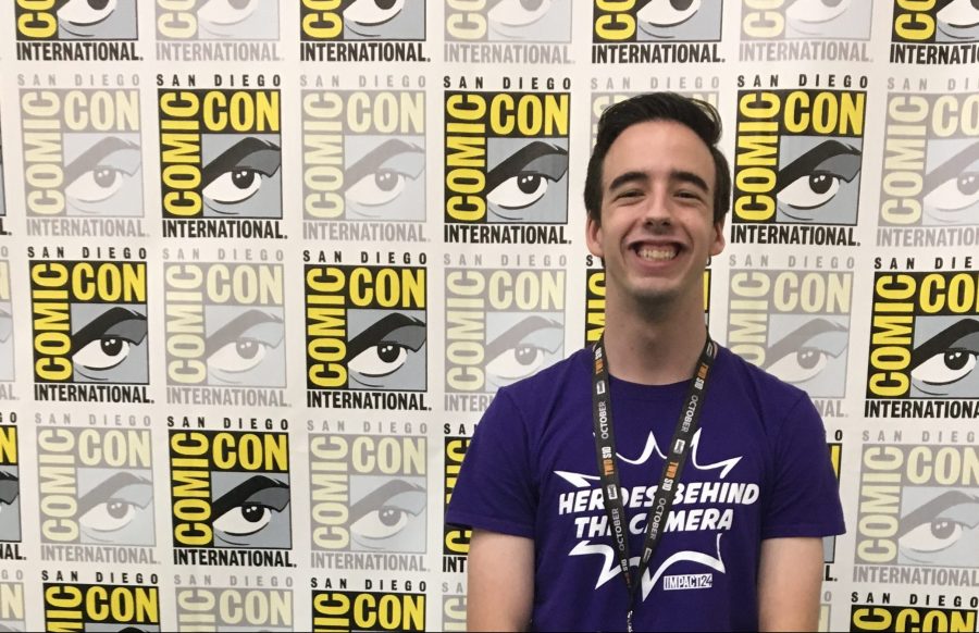 young man with short dark hair standing and smiling in front of a ComicCon backdrop