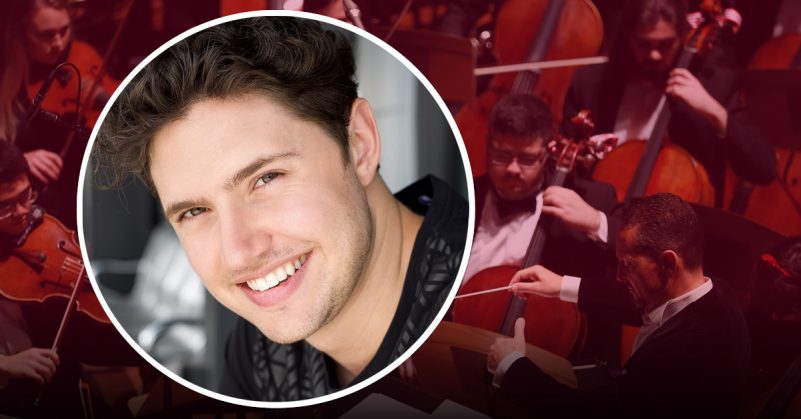 Smiling young man with short dark hair with orchestra backdrop