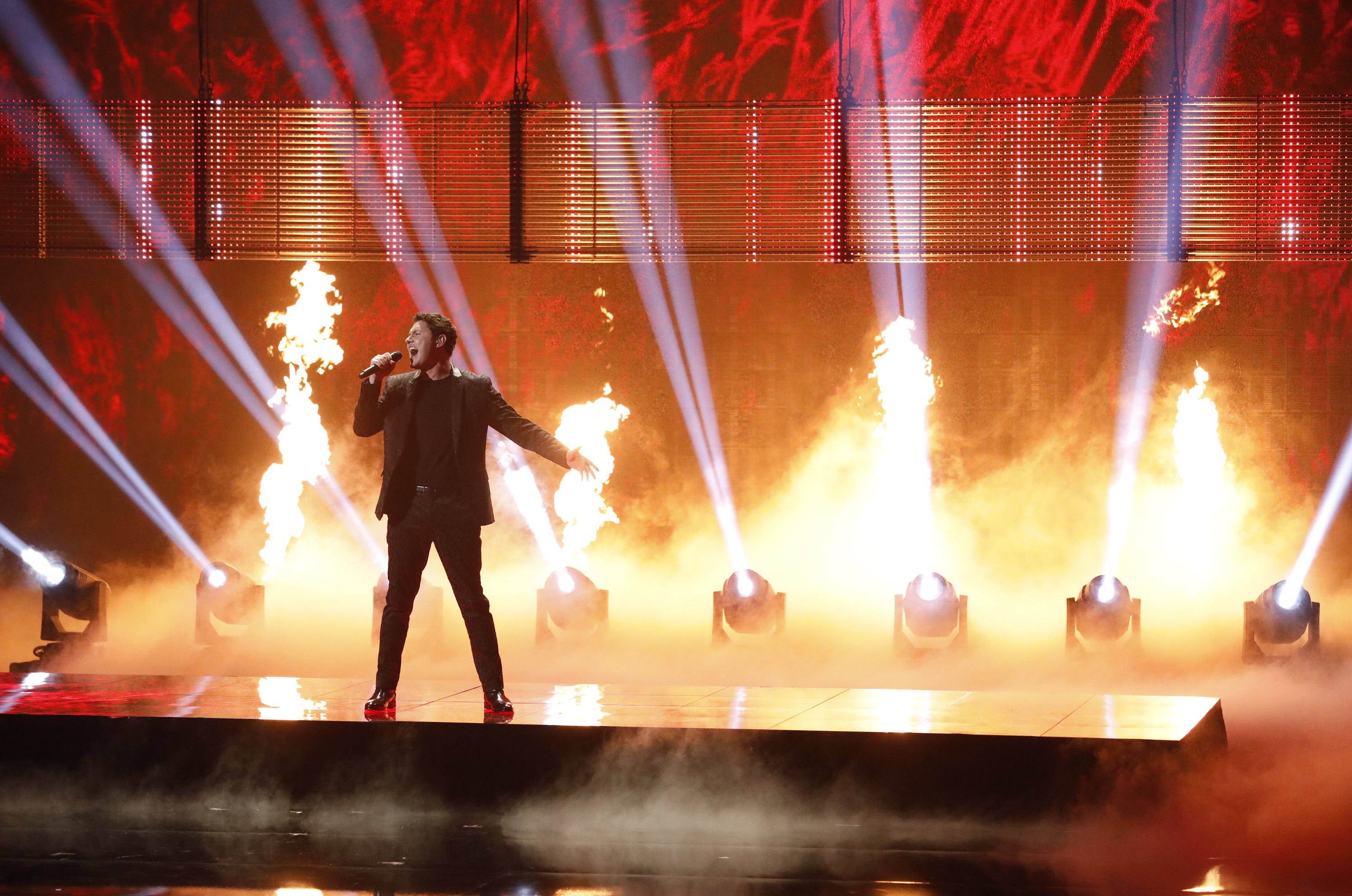 Young man singing on stage with flames in the background