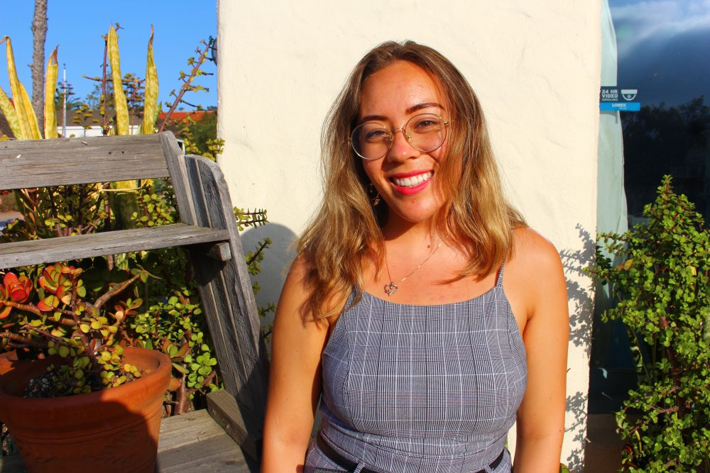 Young woman with shoulder-length blonde hair and glasses smiling on a sunny porch