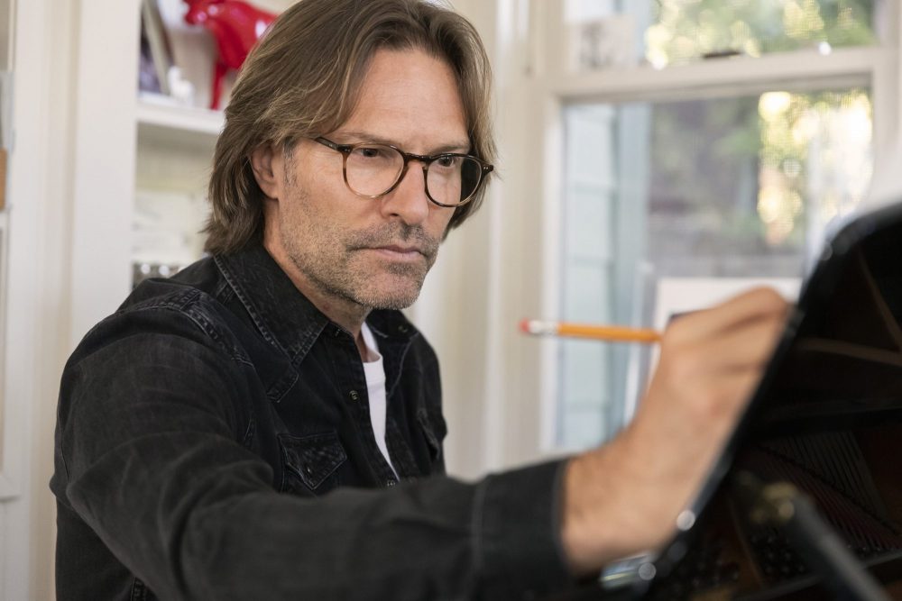 man with glasses seated at piano holding pencil