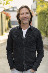 man wearing dark shirt smiling with hands in pockets