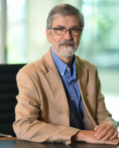 bearded man with glasses seated with hands on table
