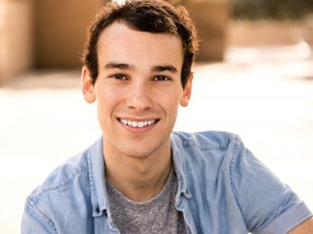young smiling Caucasian male with short dark hair in light blue button over-shirt and gray t-shirt