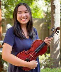 smiling woman with long dark hair in purple dress holding a violin