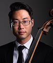 Asian-American man with glasses wearing dark suit, white dress shirt, dark tie, holding a cello