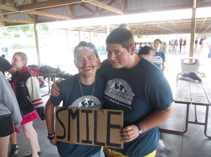 Image of two men holding a sign that reads SMILE