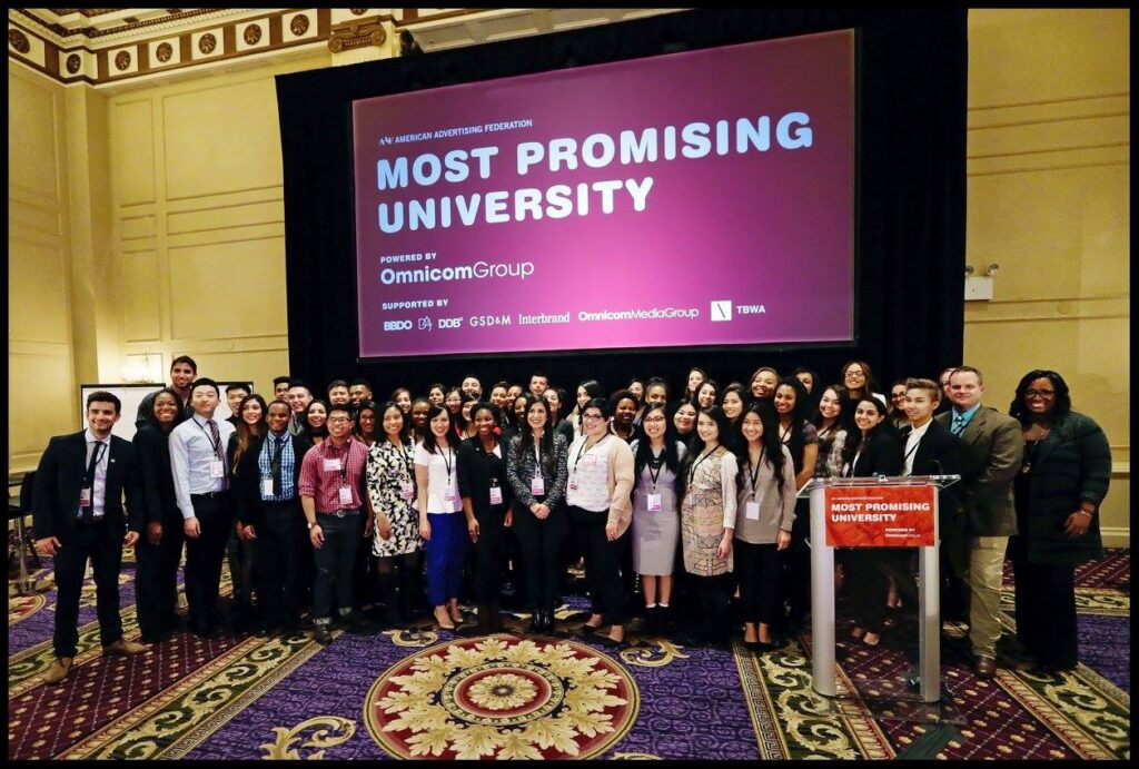 large group standing in front of a screen that says most promising university