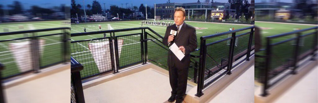 man holding microphone standing by a football field
