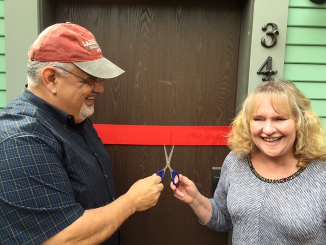 Man and woman cut ribbon in front of door.