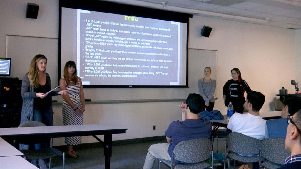 Four people in front of a screen present to a group.