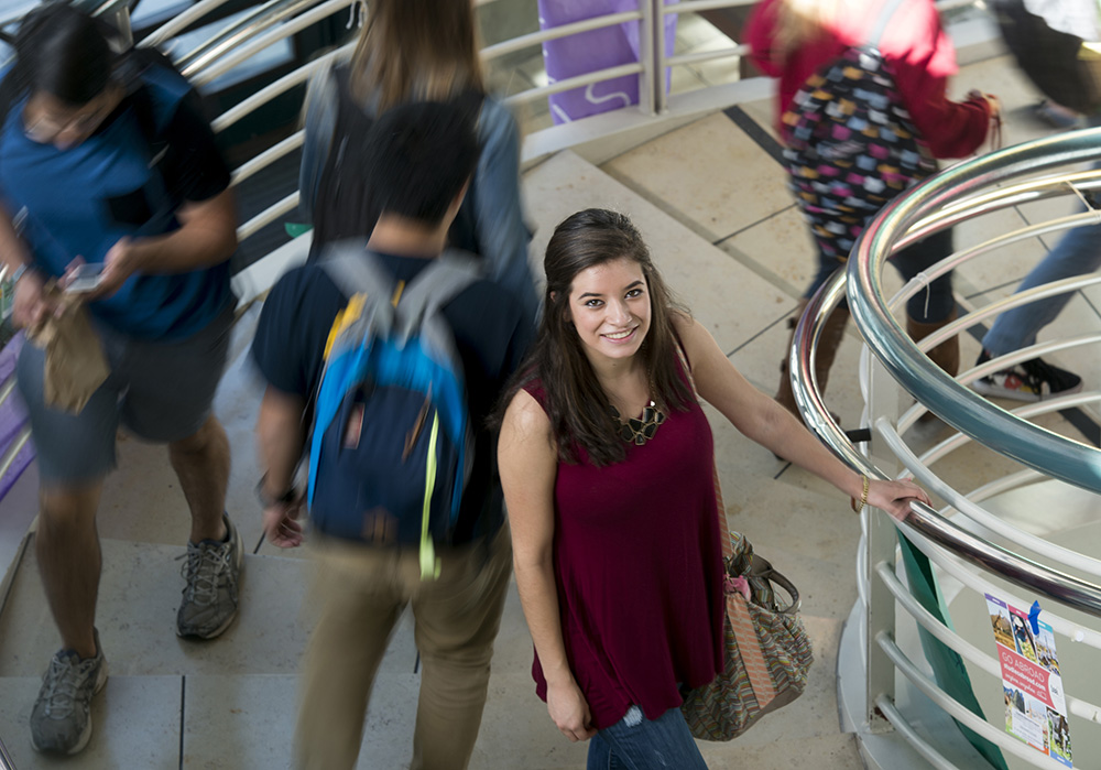 Woman standing on spiral staircase as others walk by.