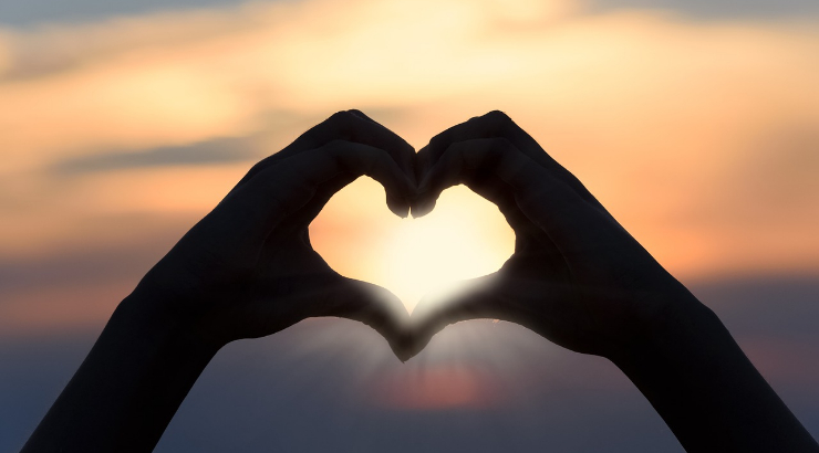 Two hands forming a heart with a sunset in the background