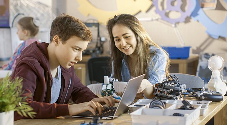High school student on a laptop with a teacher in a robotics lab
