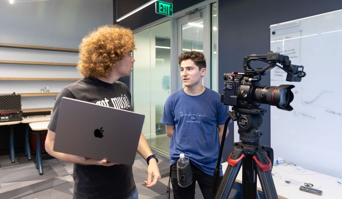 Trevor gore standing with a laptop next to Brandon Hill next to a camera.