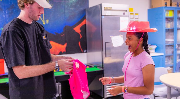 A Chapman students hands over a light-up pink Barbie vest to the very excited grade-schooler.