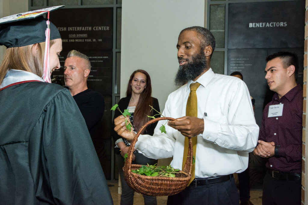 Chaplain handing out a piece of ivy to a graduate