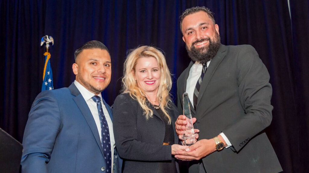 Two men and a woman wearing suits, holding a glass award