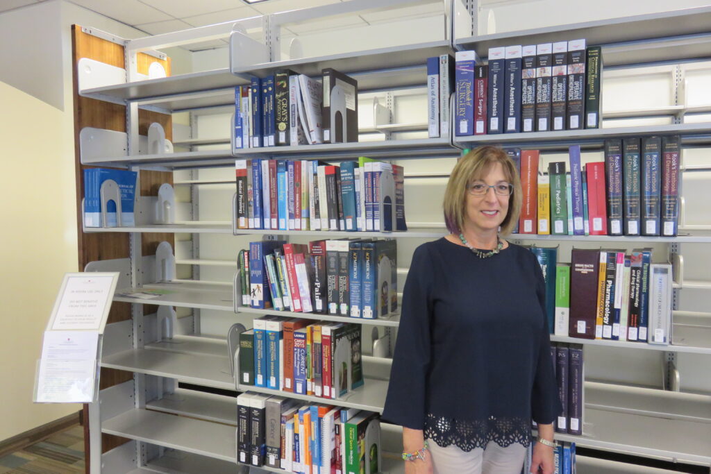 Woman standing next to books on shelf in library.