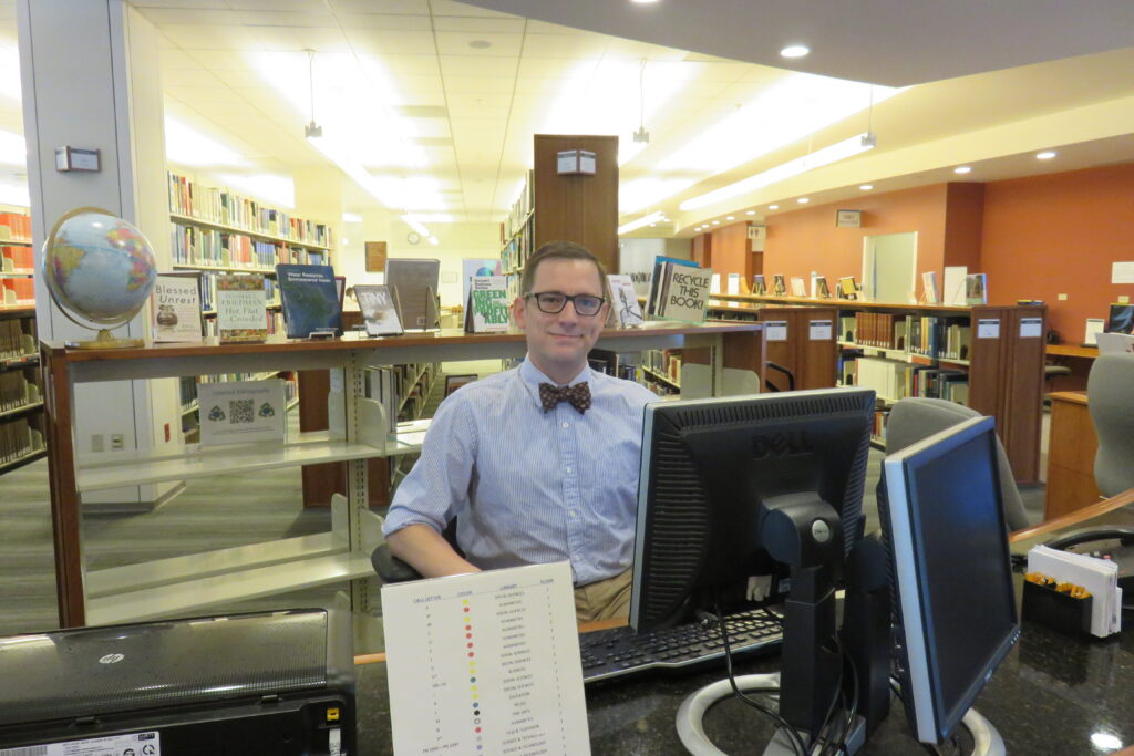Man in bowtie using computer in library.