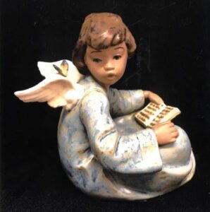 A small porcelain figurine of a seated angel reading a book,.