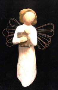 A small wooden figurine of a female angel with wire wings holding a book.