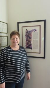 An adult woman stands next to a framed print hanging on a wall