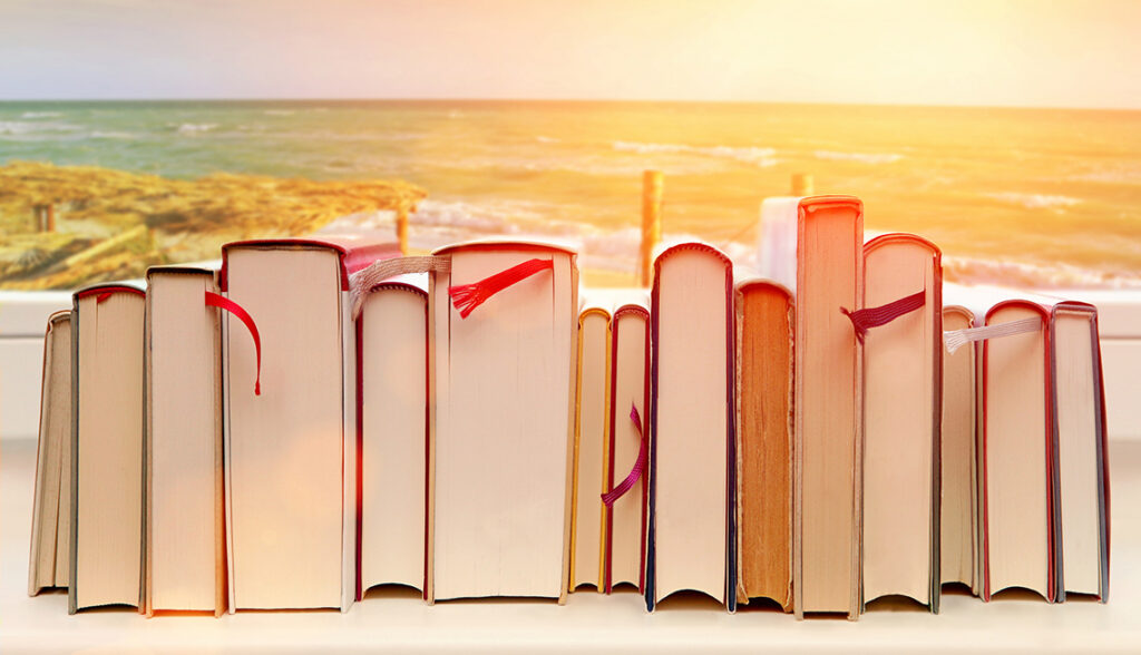 Graphic of the edge of a stack of books, horizontal, superimposed against a background of a sunset over a beach,