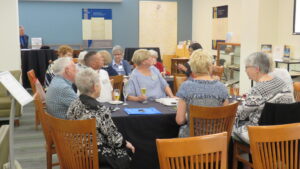 A group of people sit at tables, looking at a projector screen off-camera.