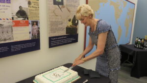 A woman stands to the right of the frame, cutting a large cake.