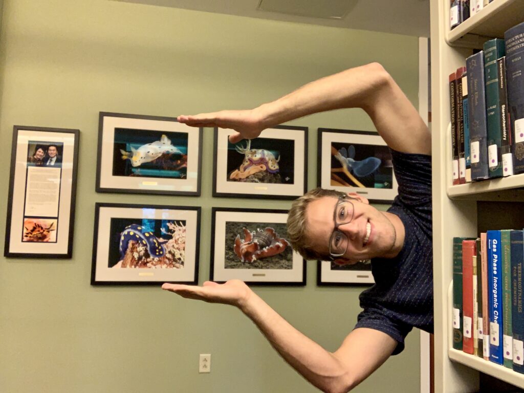 Jimmy posing sideways, as if swimming, with a wall of framed photos behind him.
