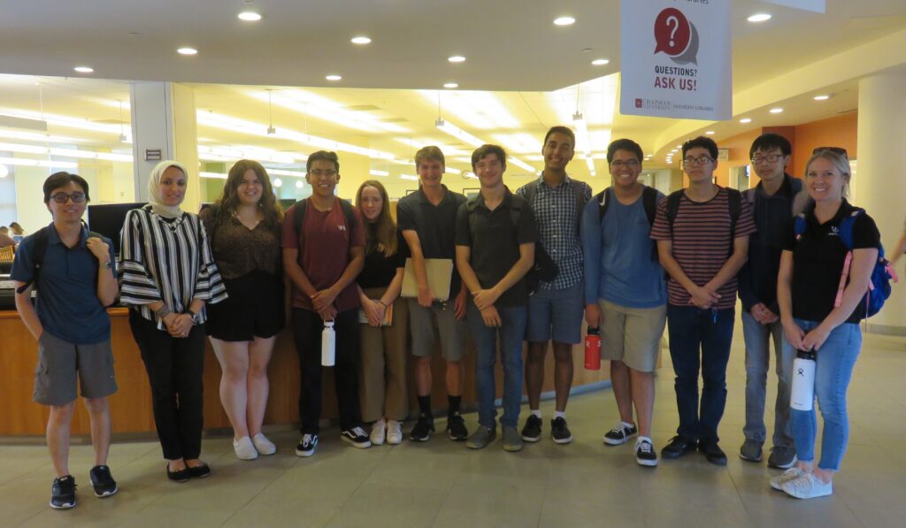 A group of twelve people, mostly high school students, stand together in a line posing for the camera