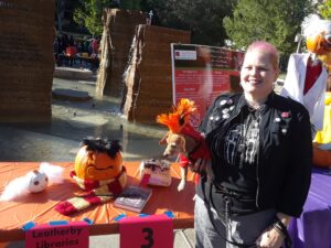 A woman and a dog, both dressed like punk rockers, stand next to the table with the decorated pumpkins