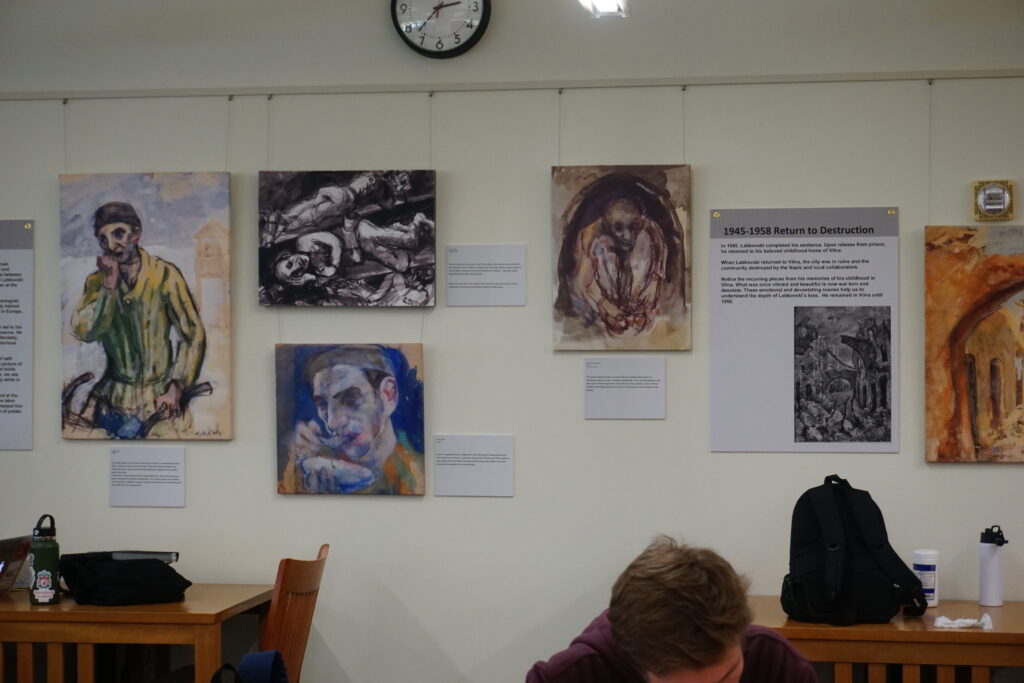 Paintings and explanatory text hanging on a wall over desks where students are studying.