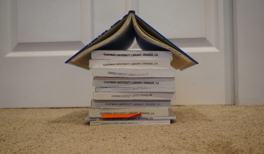 A stack of books, all facing to show their "Chapman University Library" stamps on the bottom, stacked to look like a rudimentary house