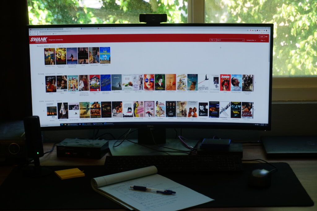 Photograph of a computer desk, with the browser on the computer screen open to the Swank website