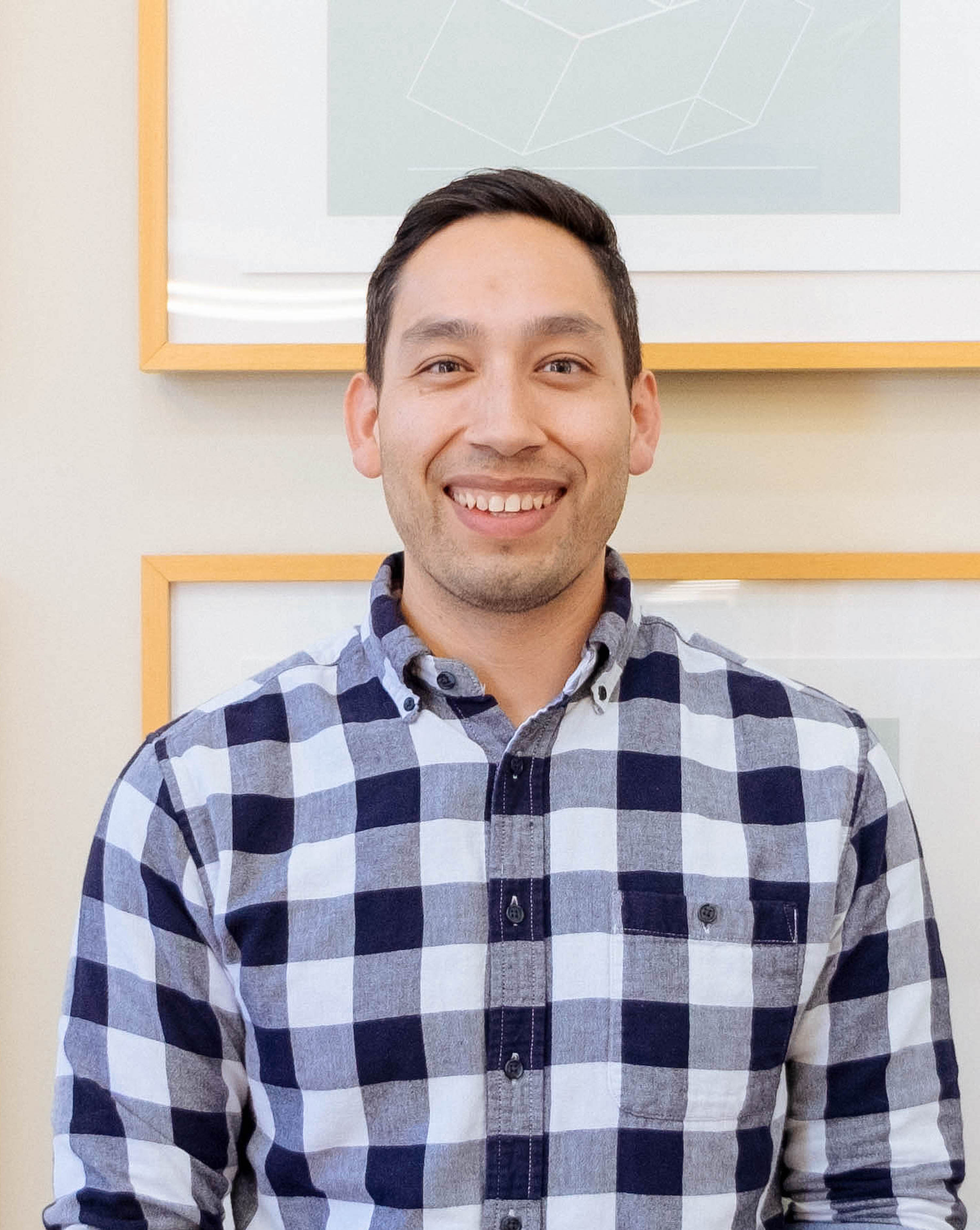 A man in a navy blue and white checked shirt smiles for the camera.