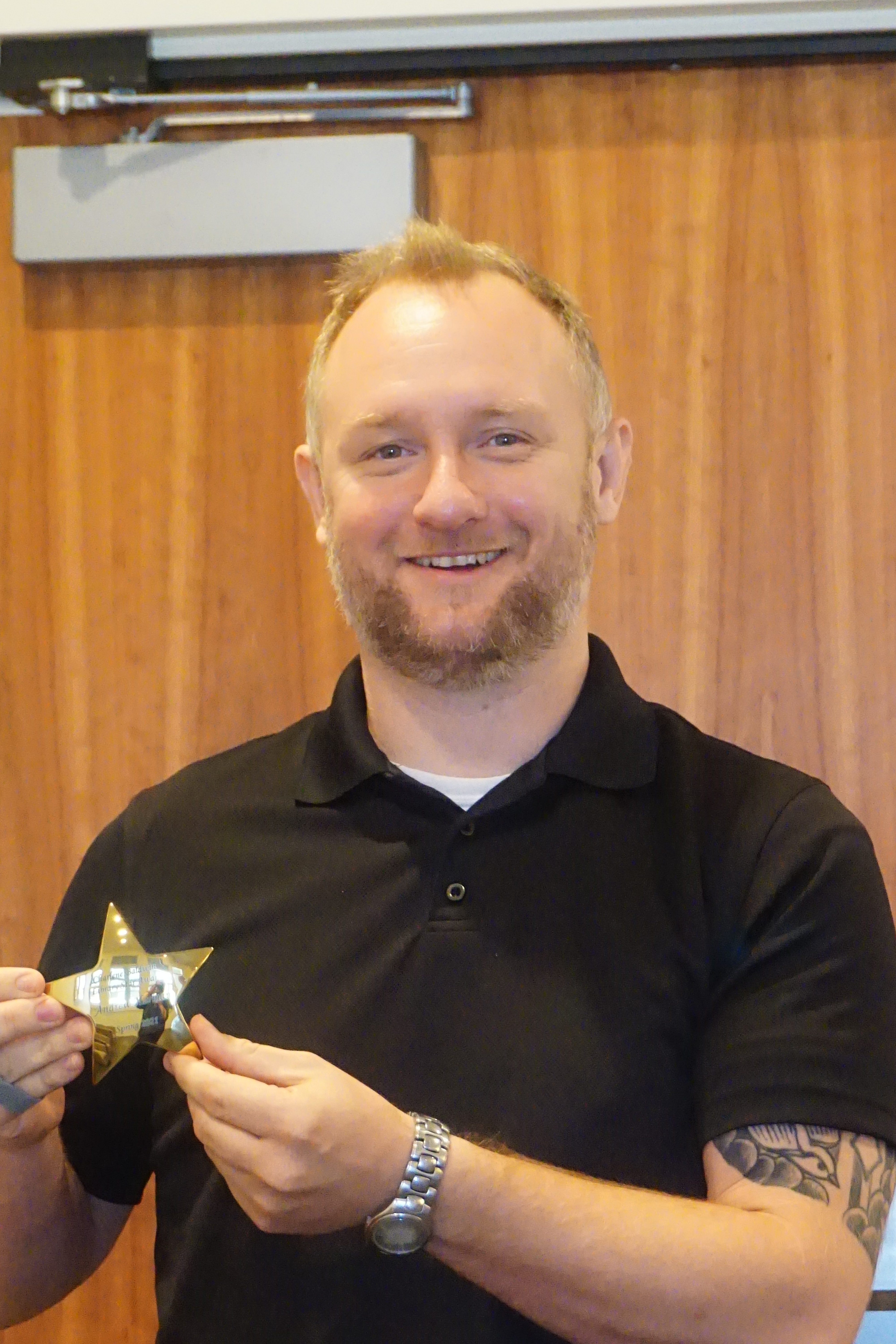 A man smiling for the camera and holding up a small gold star.