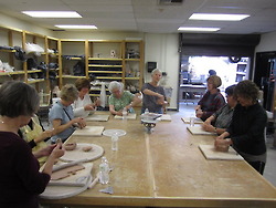 Group of people at table working on ceramics.
