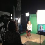 Woman being filmed in front of green screen.